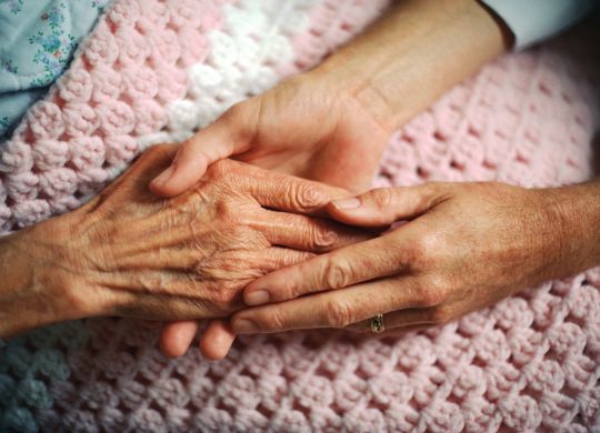 A geriatrician holds the hand of an elderly woman with arthritis.