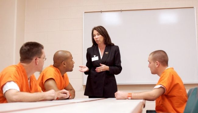 woman helping three inmates in a classroom setting