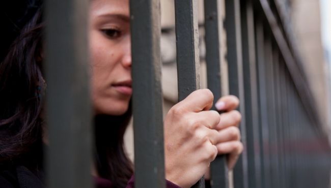 woman standing behind and holding prison bars