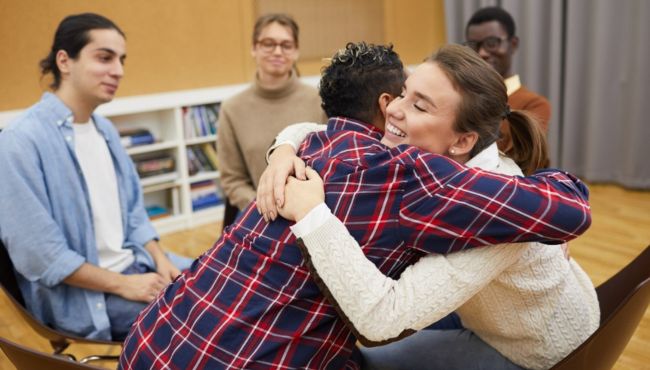 two people in a group counseling setting hugging and smiling