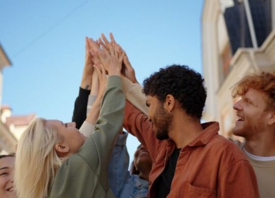 group of young adults standing in a group smiling and with their hands together in the hair in celebration or unity