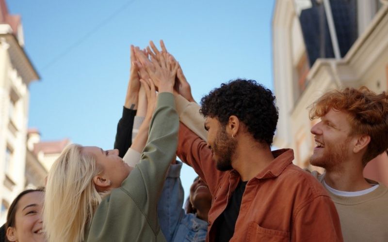 group of young adults standing in a group smiling and with their hands together in the hair in celebration or unity