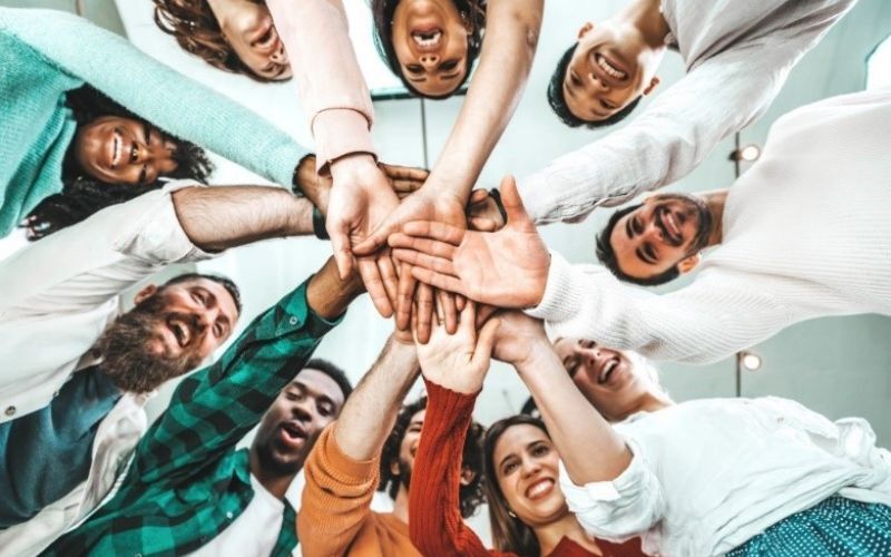 group of people in a circle with their hands meeting in the middle and smiling